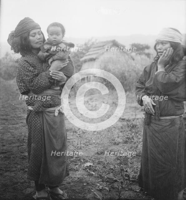 Two Ainu woman, one holding a child, standing outside, 1908. Creator: Arnold Genthe.