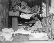 Javanese(?) woman sitting in room working with textiles at exhibit featuring foreign..., 1892. Creator: Frances Benjamin Johnston.