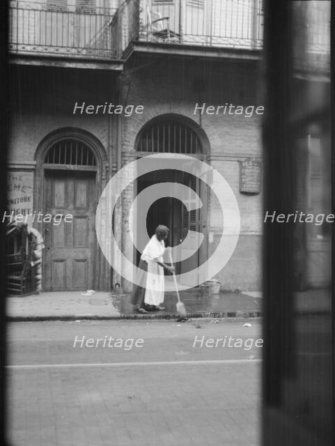 View from across street of a woman cleaning the sidewalk, New Orleans, between 1920 and 1926. Creator: Arnold Genthe.