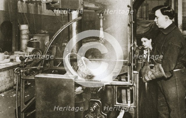 Making money; lowering a pot of liquid metal into a machine, 20th century. Artist: Unknown