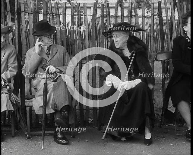 An Elderly Woman Wearing a Wide Hat, a Fur Stole, and Holding a Walking Stick Sitting on a..., 1938. Creator: British Pathe Ltd.