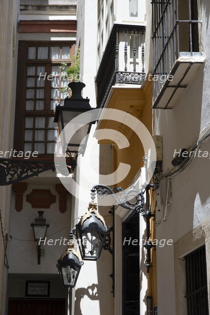 Narrow street with old lamps and balconies in the pedestrian area of Seville, Spain, 2023. Creator: Ethel Davies.