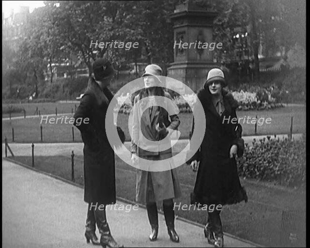 Three Female Civilians Wearing Glamorous Outfits and Long Boots Walking on a Park, 1920. Creator: British Pathe Ltd.