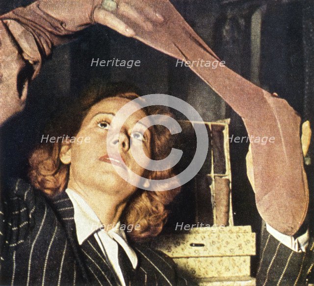 A woman in Paris examines a pair of silk stockings, 1941 Artist: Unknown