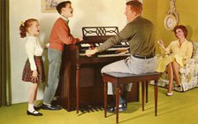 Family singing around a Wurlitizer organ as father plays, De Kalb, Illinois, USA, 1962. Artist: Unknown