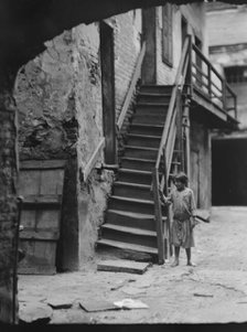 Child standing next to a stairway in a courtyard, New Orleans, between 1920 and 1926. Creator: Arnold Genthe.