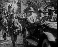 Crowd Chasing a Motorcar as It Climbs up a Hilly Cobbled Street, 1920. Creator: British Pathe Ltd.