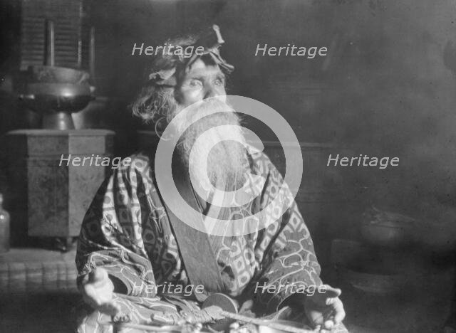 Ainu chief wearing a headdress seated with a sword in his lap, 1908. Creator: Arnold Genthe.