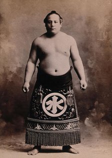 A young sumo wrestler posing in a photographic studio, wearing a richly decorated apron..., c1900. Creator: Unknown.