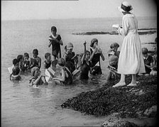 Children Having Swimming Lessons in the Sea While the Teacher Stands on a Rock, 1921. Creator: British Pathe Ltd.