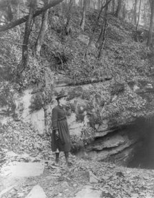 Frances Benjamin Johnston, full, standing by wooded cliff at entrance to Mammoth Cave, (c1891?). Creator: Frances Benjamin Johnston.