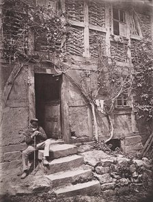 [Man Sitting on Steps of House with Socks Hanging on Nearby Vine to Dry], 1880s. Creator: Unknown.