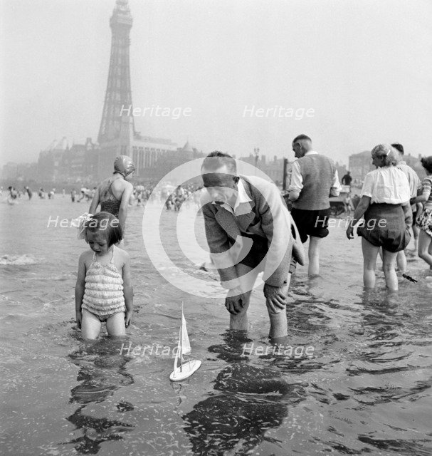 A father and daughter sail a model yacht in the sea, Blackpool, c1946-1955. Artist: John Gay