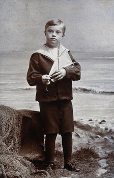 A boy with Down's syndrome, dressed in a sailor suit, standing against a nautical... Creator: Kent Coast Studio.