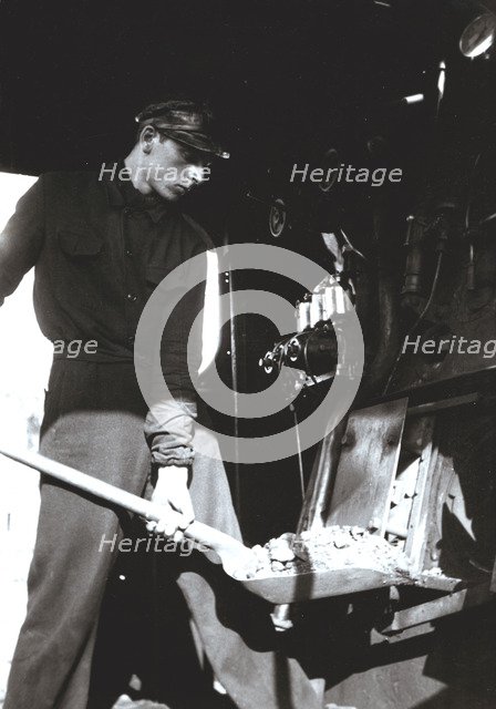 Stoker putting coal to a steam train engine.