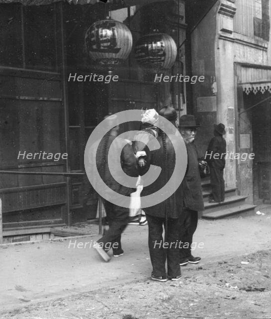 Men standing or walking down a sidewalk, Chinatown, San Francisco, between 1896 and 1906. Creator: Arnold Genthe.