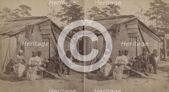 Family group sitting in front of a wooden shack, (1868-1900?). Creator: Unknown.