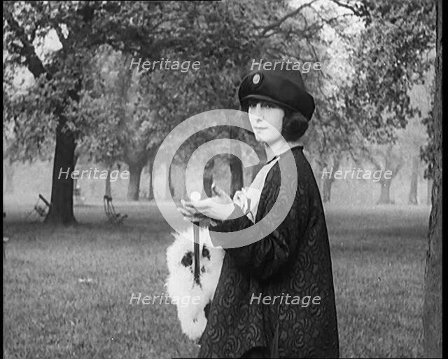 Female Civilian Dressed Glamorously Holding a Fur Trimmed Parasol in a Park, 1920. Creator: British Pathe Ltd.