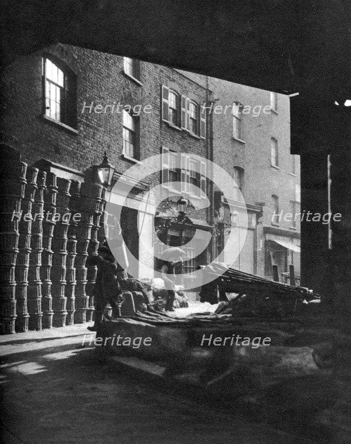 Fruit baskets piled against houses at Borough Market, London, 1926-1927.Artist: Whiffin