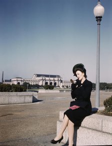 Woman putting on her lipstick in a park with Union Station behind her, Washington, D.C., ca. 1943. Creator: Unknown.