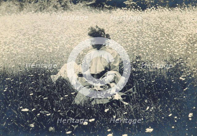 Woman with wreath of leaves in her hair sitting in a field of daisies, c1900. Creator: Unknown.