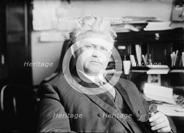 H.T. Rainey, holding bifocals, at desk, 1911. Creator: Bain News Service.
