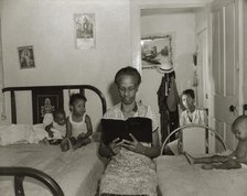 Mrs. Ella Watson, a government charwoman, reading the Bible to her household, Washington, DC, 1942. Creator: Gordon Parks.