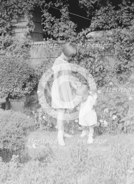 Children of Mrs. George Eustis standing outdoors in a garden, between 1911 and 1942. Creator: Arnold Genthe.