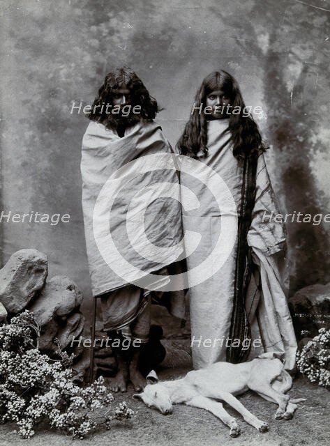A man and woman of the Toda tribe standing in a photographic studio, with a dog lying..., c1900. Creator: Unknown.