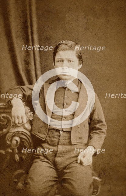 A seated young man with clenched fists, leaning against an ornate table, c1890s. Creator: AE Scales.