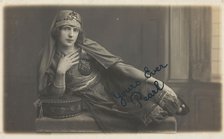 A man in drag, poses wearing delicate attire; curled up on a piece of furniture, [1910-1919?]. Creator: Unknown.