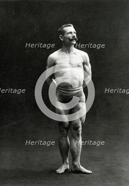 A male bodybuilder wearing bathing trunks, posing in a studio setting, between 1899 and 1908. Creator: Unknown.