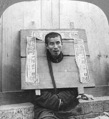 'Chinese prisoner in the cangue placarded with the record of his crime', China, 1902. Artist: CH Graves