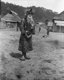 Ainu chief wearing a headdress standing in the village lane, 1908. Creator: Arnold Genthe.