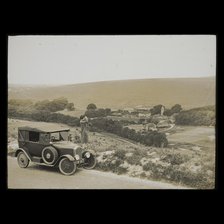 A woman standing beside a car parked on East Dean Road near Exceat Hill, looking out..., 1921-1939. Creator: Norman Kingsley Harrison.
